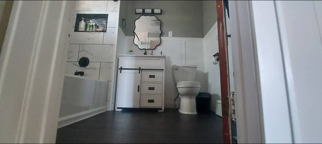 Completed bathroom with tiled tub surround, barn-door vanity, and new toilet