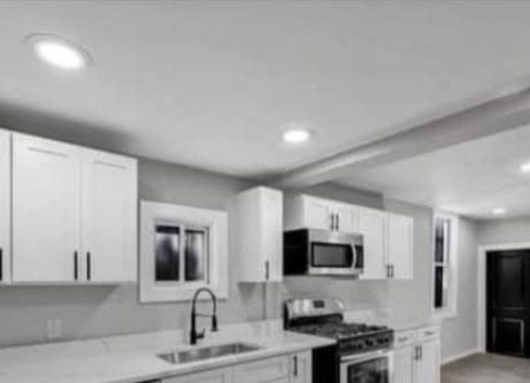 Same kitchen finished, with white shaker cabinets, quartz counters, tile backsplash, and new stainless appliances