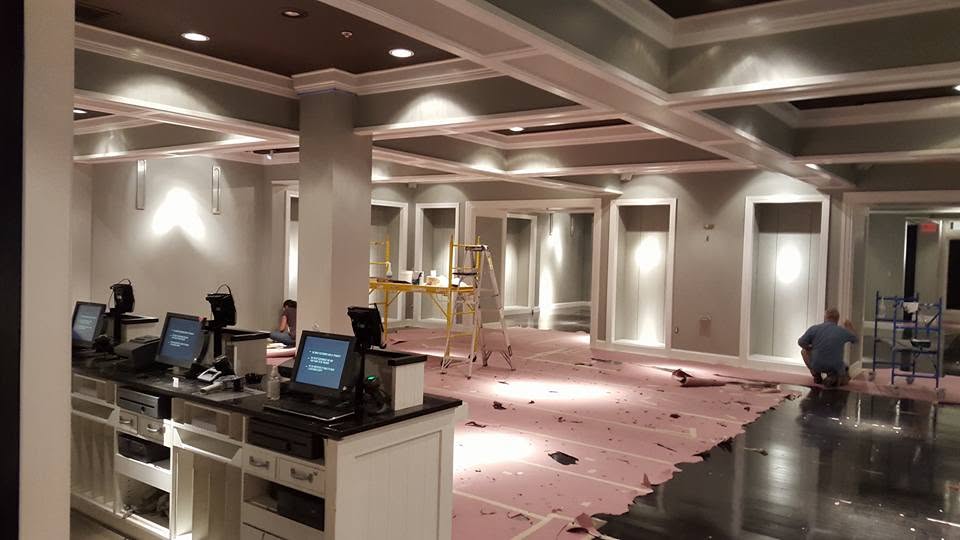 Commercial interior buildout with custom coffered ceiling millwork, recessed lighting, and a service counter, mid-installation with floor protection down