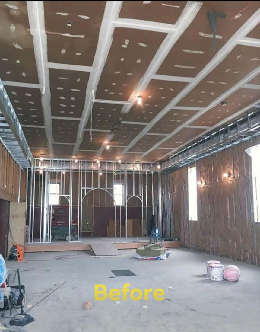 Large assembly hall gutted to framing and drywall, with metal stud walls and ceiling rough-in exposed, mid-renovation