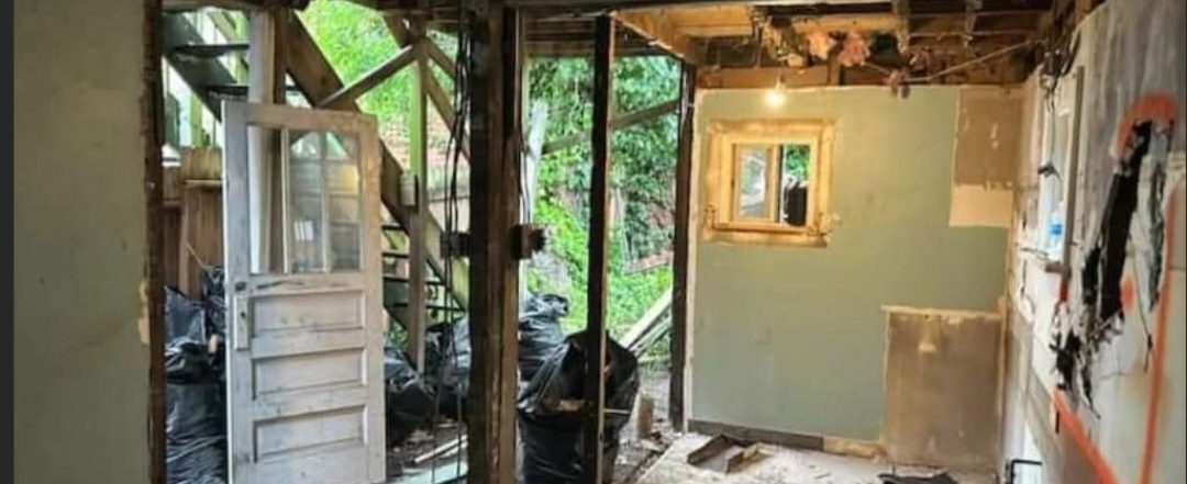 Kitchen gutted to framing, with an old exterior door removed and studs exposed, at the start of a full remodel