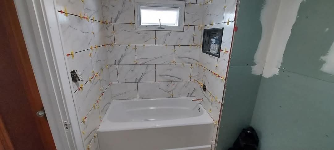 Bathtub surround partway through marble-look tile installation with spacers still in place